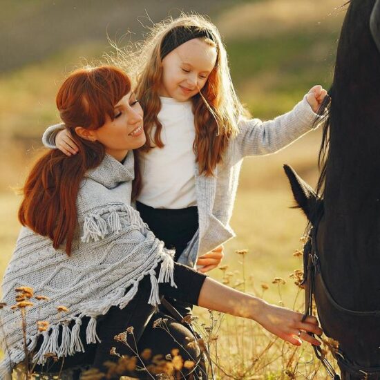 Mother and daughter next to horse. Little girl in a summer field. Family playing with a horse