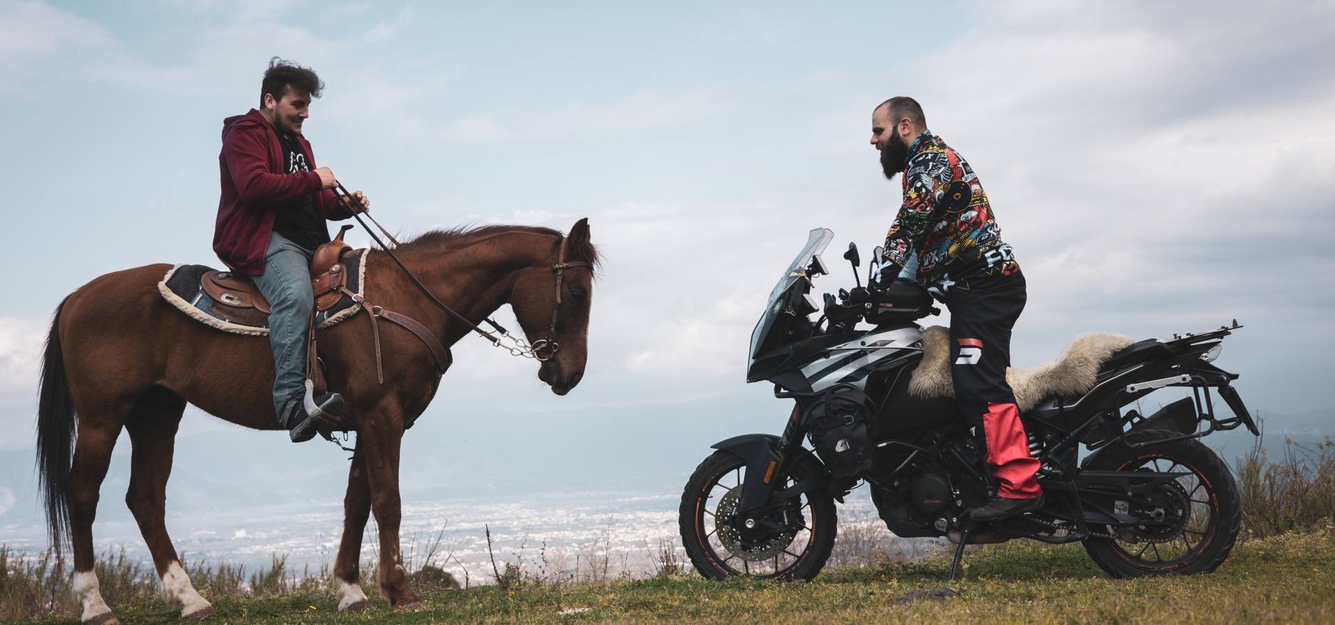 motociclista su una moto che sta di fronte un cavallo con il suo cavaliere con un paesaggio verdeggiante